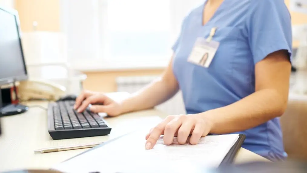 Nurse reviewing paperwork and entering into a computer