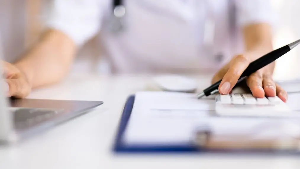 Medical office worker at desk with laptop and calculator